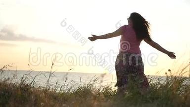一个年轻的女孩正在<strong>草地</strong>上，在夕阳和<strong>大海</strong>的背景下旋转，享受着阳光。 1920x1080